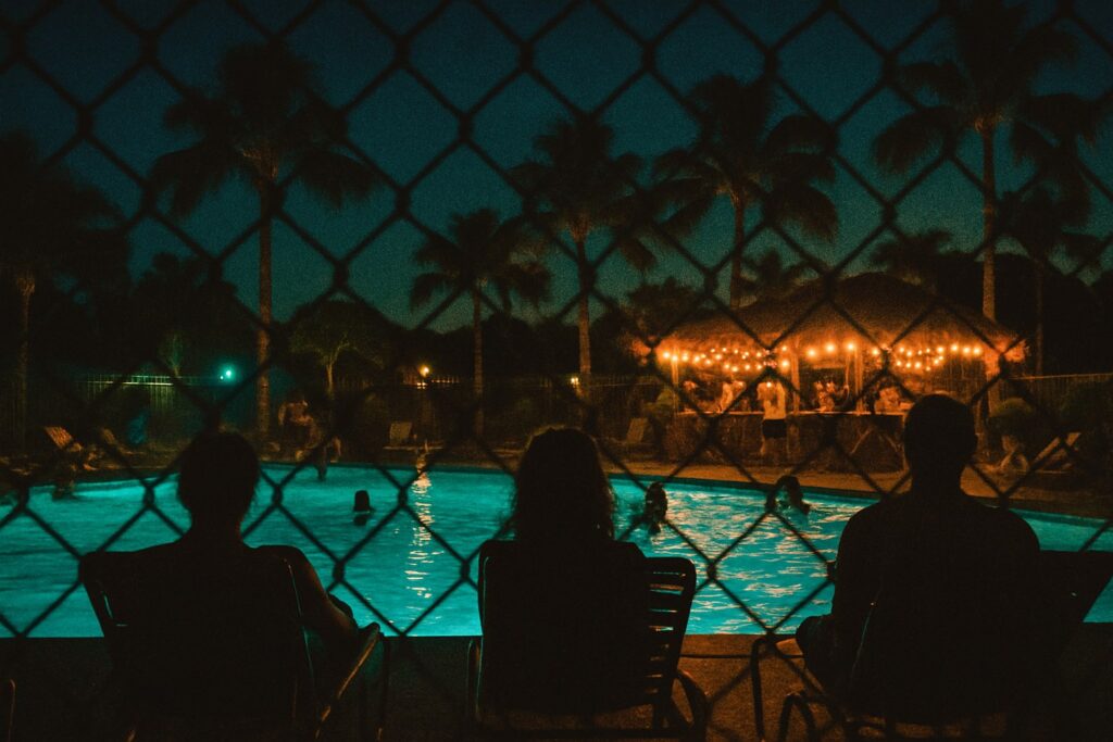 Silhouettes of people by a lit pool at night