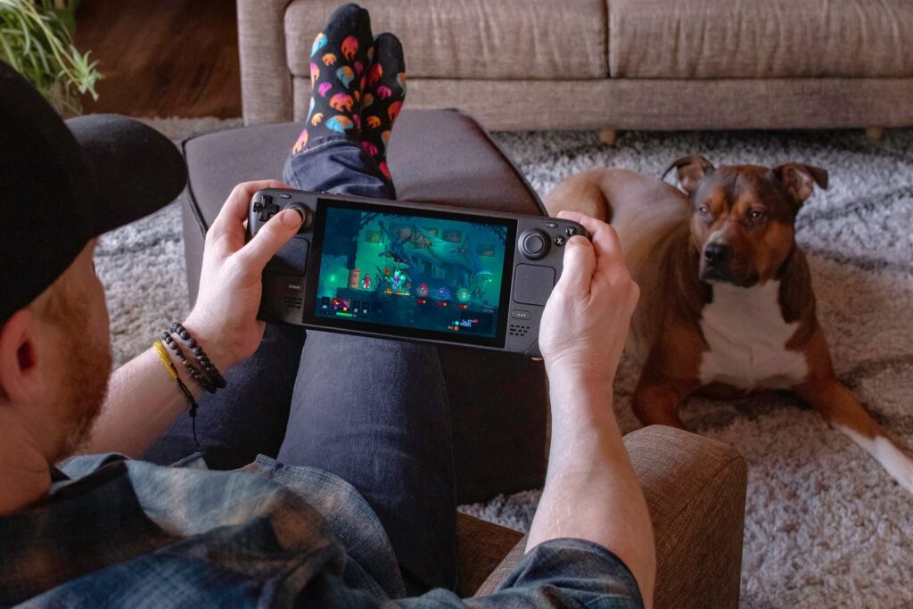 A person playing a game on a Steam Deck at home next to a dog
