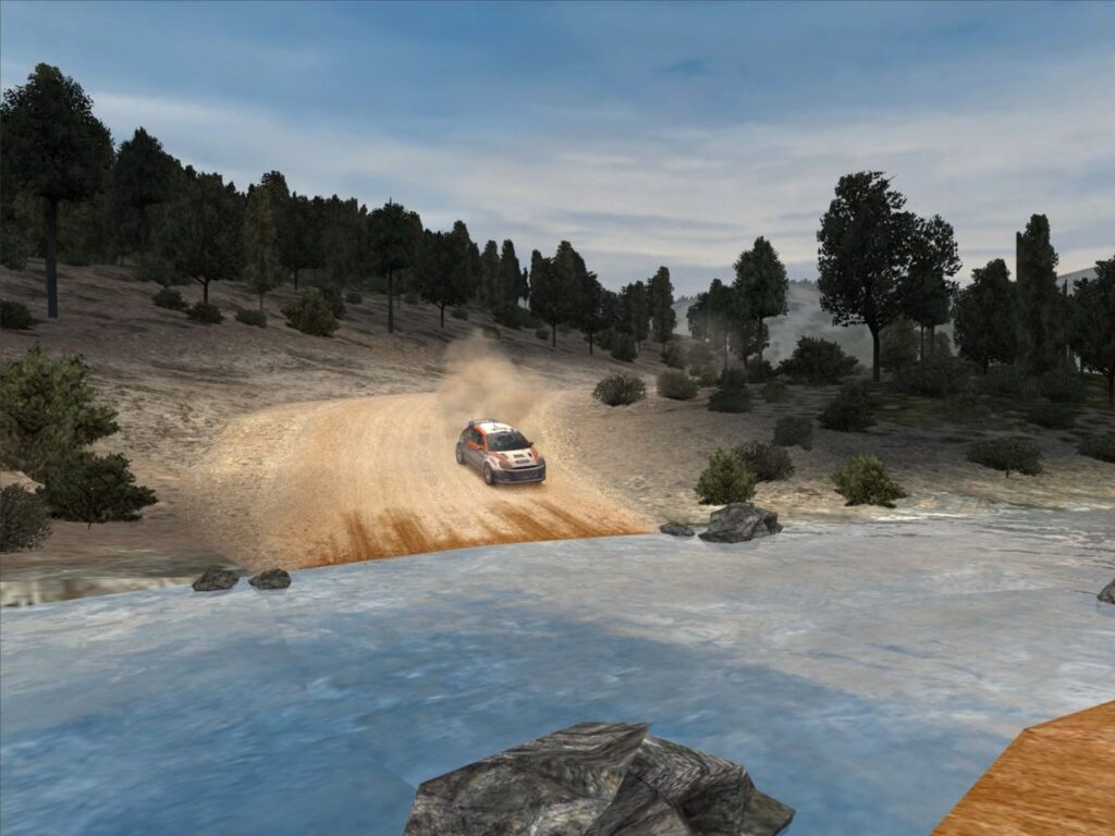 A rally car kicks up dust on the way down to a river, aerial view over a gravel track and a rocky bank