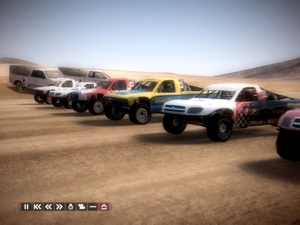 A row of pickups and off-roaders lined up at the start on a dusty plain