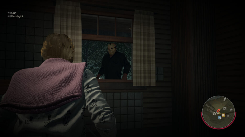 A counselor in a pink jacket looks out of a cabin window, with Jason standing behind the glass