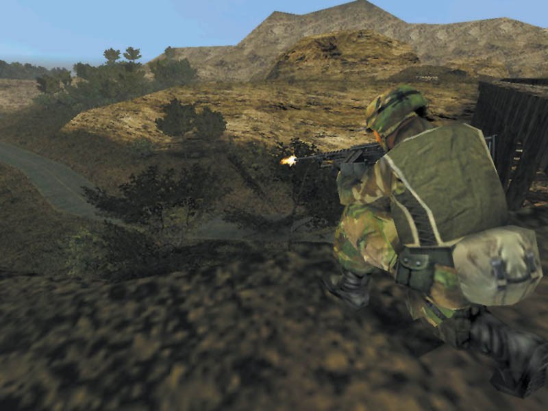 Een soldaat met helm en camouflage schiet vanachter rotsen op een heuvel met een paar bomen